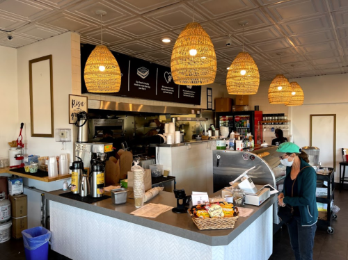 A cozy café interior with woven light fixtures, a counter, and a staff member preparing orders.
