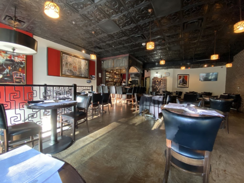 Interior of a restaurant featuring dark wood furniture, decorative ceiling, and warm lighting, with tables set for dining.