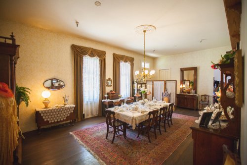 A vintage dining room with a long table set for a meal, elegant decor, and warm lighting.