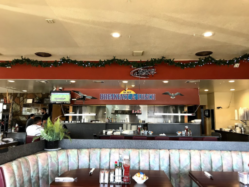 Interior of a cozy diner with a breakfast and lunch sign, festive decorations, and booths for seating.