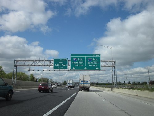 Highway exit signs for Joliet Road and directions to Southwest and Northwest suburbs, with vehicles on the road.