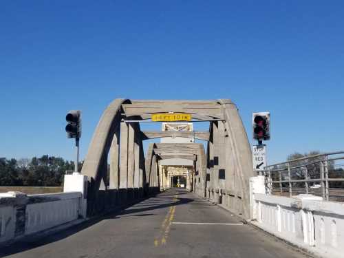 A view of a bridge with traffic lights and a height clearance sign against a clear blue sky.