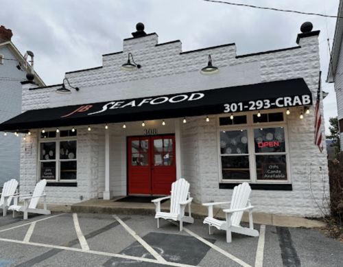A seafood restaurant with a black awning, red doors, and white chairs outside, featuring an "OPEN" sign.
