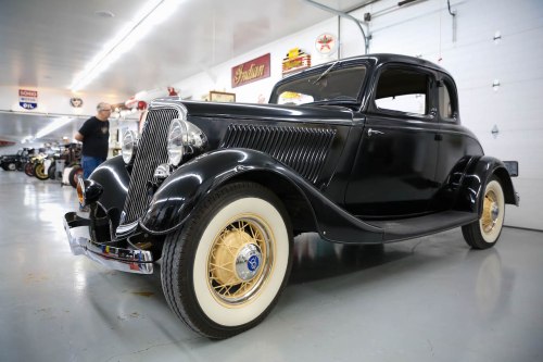 A classic black coupe car with whitewall tires, displayed in a vintage car museum.