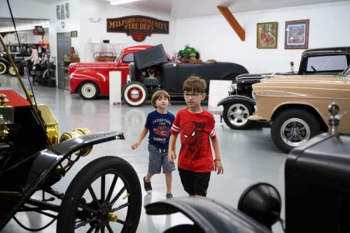 Two children walk through a vintage car museum, surrounded by classic cars and memorabilia.