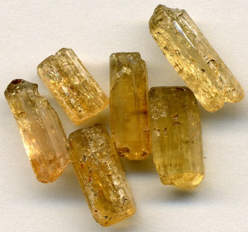 A collection of six translucent yellowish crystals arranged on a light background.