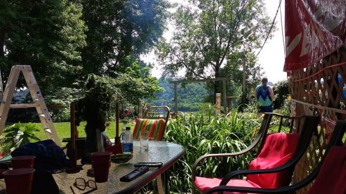 A sunny outdoor scene with chairs, a table, and greenery, featuring a ladder and a person in the background.