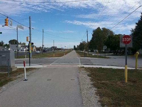 A wide, empty road with a stop sign and crosswalk, under a blue sky with scattered clouds.