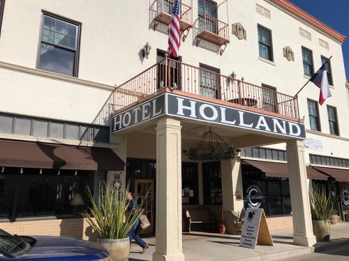 Exterior of Hotel Holland featuring a sign, flags, and a welcoming entrance with potted plants.