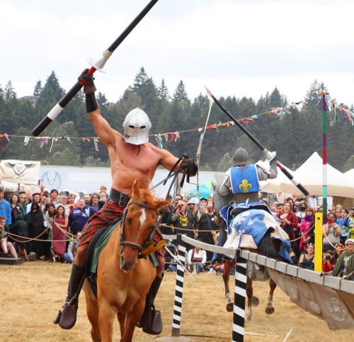 A shirtless knight on horseback raises a lance, competing in a jousting event with spectators in the background.