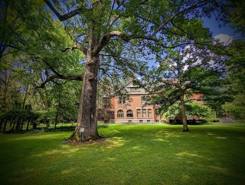 A large brick house surrounded by lush green trees and grass under a clear blue sky.