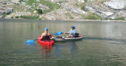 Two people kayaking on a calm lake surrounded by rocky hills, enjoying a sunny day outdoors.