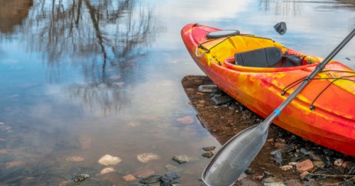 A kayak with a paddle sits on a rocky shore, and in low water, in an Indiana lake.
