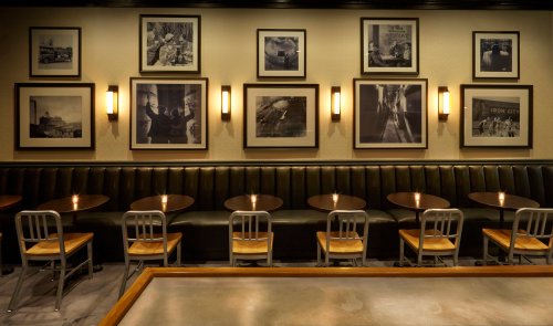 A cozy restaurant interior featuring dark leather seating, wooden tables, and framed black-and-white photos on the wall.
