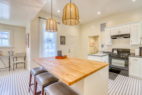 Bright kitchen featuring a wooden island, bar stools, and pendant lights, with black and white tiled flooring.