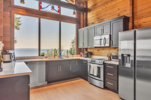 Modern kitchen with dark cabinets, stainless steel appliances, and large windows showcasing a scenic view of the water.