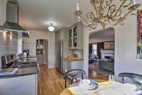 Bright kitchen with modern appliances, a dining table set for two, and a stylish chandelier overhead. Cozy living area visible.
