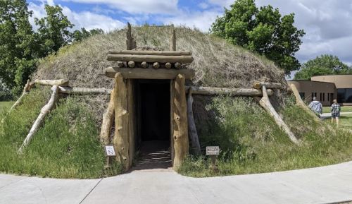 A grassy, dome-shaped structure with a wooden entrance, surrounded by trees and a pathway.