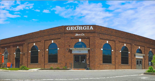 A brick building with large arched windows, featuring the sign "Georgia Beer Co" on a clear blue sky day.