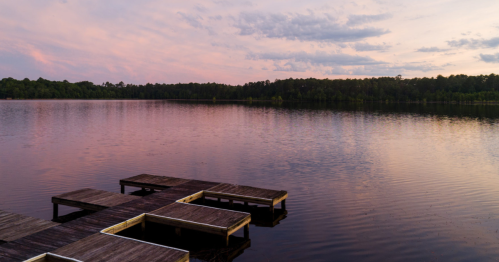 A serene lake at sunset, with wooden docks extending into the calm water and a colorful sky reflecting on the surface.