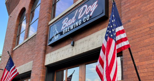 Sign for Bad Dog Brewing Co. on a brick building, with American flags displayed on either side.
