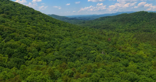 Lush green mountains and valleys under a bright blue sky with scattered clouds.