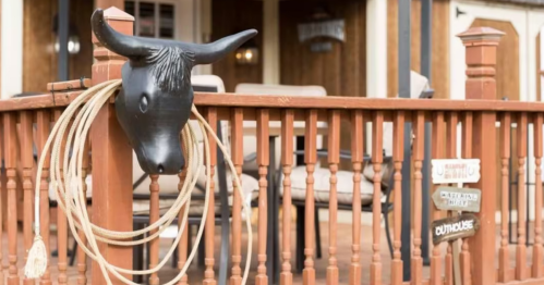 A wooden railing with a bull head sculpture and a lasso, set in a rustic outdoor space with seating.