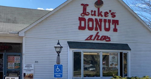 A white building with a sign reading "Luke's Donut Shop," featuring a window display and accessible parking.