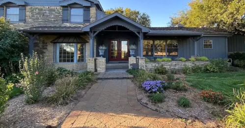 A charming house with stone and wood exterior, surrounded by a landscaped garden and pathway leading to the entrance.