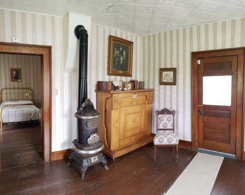A cozy room with a vintage stove, wooden furniture, and a doorway leading to a bedroom.