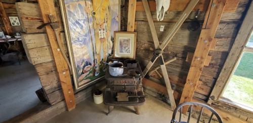 A rustic interior featuring a vintage stove, framed artwork, and wooden walls, creating a cozy, historical atmosphere.