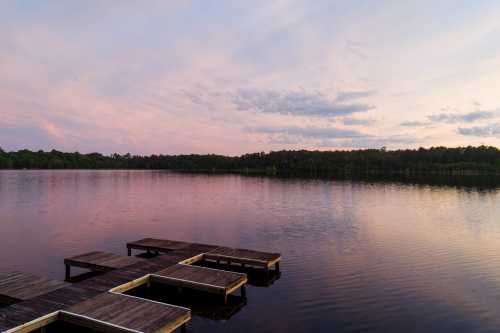 A serene lake at sunset, with a wooden dock extending into the calm water and colorful clouds reflecting above.