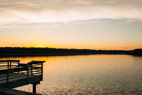 A serene lake at sunset, with golden reflections on the water and a wooden dock in the foreground.