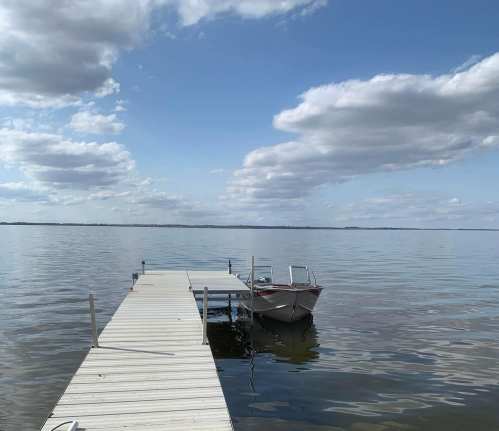 A calm lake scene with a wooden dock and a small boat under a blue sky with fluffy clouds.