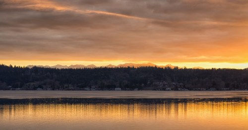 Sunset over a calm lake, with mountains in the background and a golden reflection on the water.