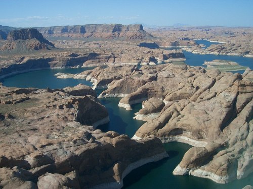 Aerial view of rugged, rocky terrain with winding blue waterways and distant hills under a clear blue sky.