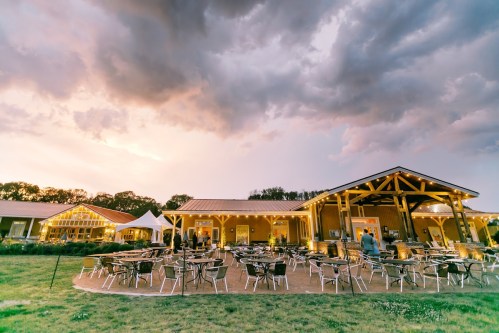 A spacious outdoor dining area with tables and chairs, set against a dramatic sky at sunset.