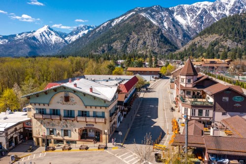 Aerial view of a charming alpine village with mountains in the background and colorful buildings lining the street.