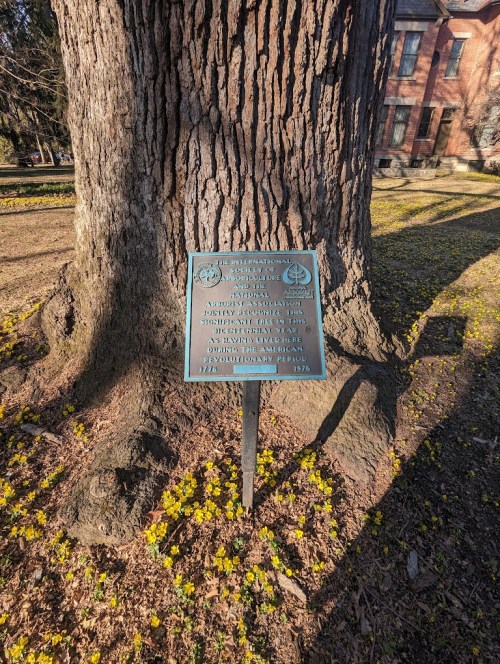 A plaque on a tree commemorating the American Revolutionary War and honoring historical figures.