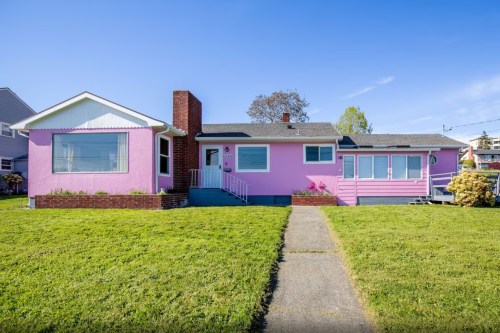 A bright pink house with a green lawn and a walkway leading to the entrance, under a clear blue sky.