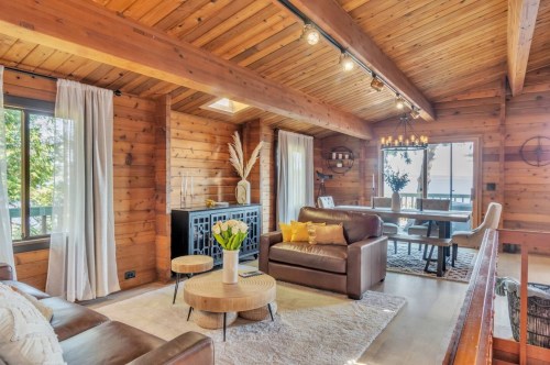 Cozy wooden living room with a leather sofa, round coffee table, and dining area, featuring large windows and warm lighting.