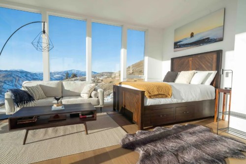 Modern bedroom with large windows, mountain views, a cozy bed, sofa, and stylish decor.