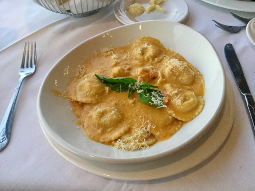 A plate of ravioli in a creamy sauce, garnished with basil and grated cheese, on a white tablecloth.