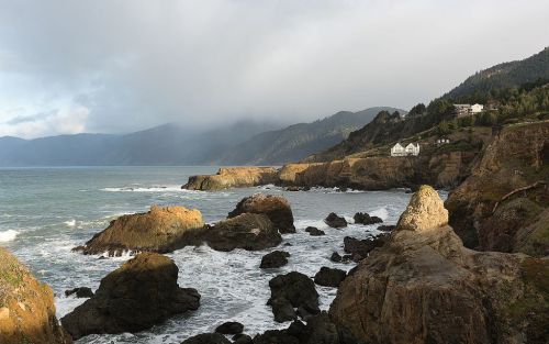 A coastal landscape featuring rocky cliffs, waves crashing, and misty mountains in the background.