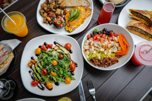 A variety of colorful dishes including salads, potatoes, wraps, and drinks arranged on a wooden table.