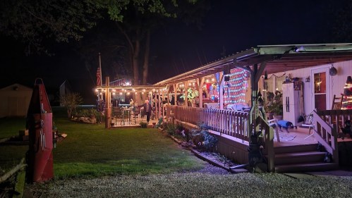 A cozy outdoor space at night, decorated with colorful lights, featuring a porch and a well-lit garden area.