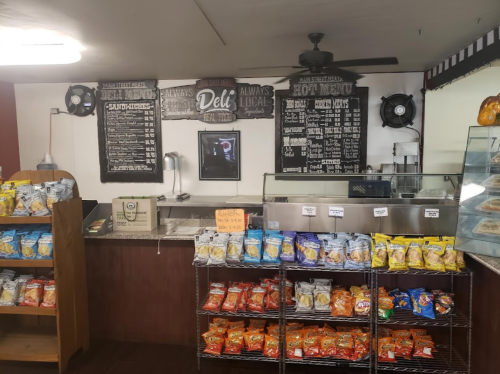 A deli counter with menus on the wall, snack shelves, and a display case in a cozy, well-lit setting.