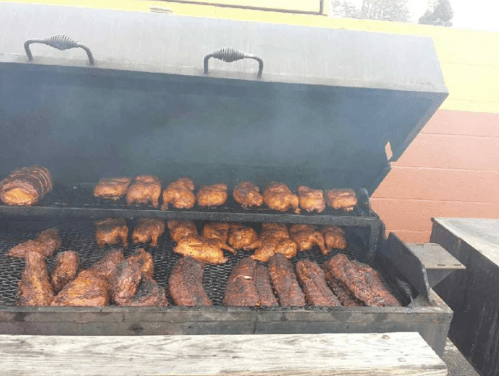 A large barbecue grill filled with various meats, including chicken and ribs, surrounded by smoke.