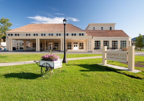 Exterior view of Mammoth Hot Springs Hotel, featuring a landscaped lawn and a sign, under a clear blue sky.