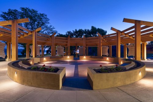 A circular outdoor space with wooden beams, soft lighting, and flower beds, set against a twilight sky.